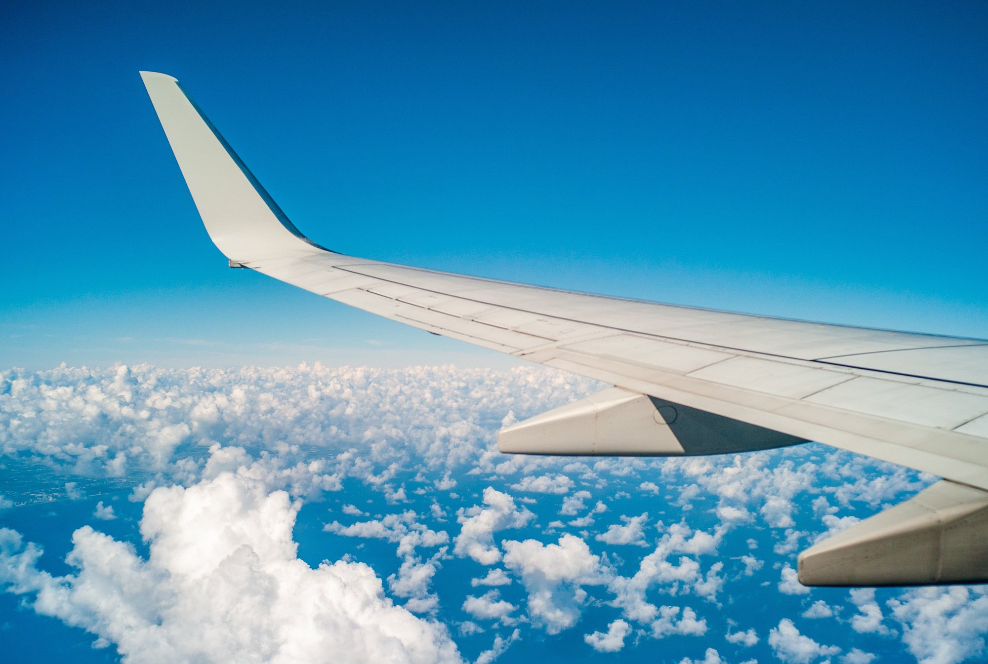 View of an airplane wing against a backdrop of a clear blue sky and scattered white clouds