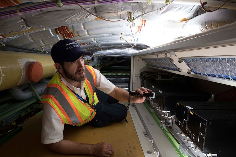 Man in high-visibility vest and cap working in a confined technical space with electronic equipment and cables